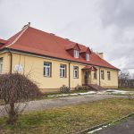 Budynek szkolny z czerwonym dachem. Ściany elewacji pomalowane na żółto.